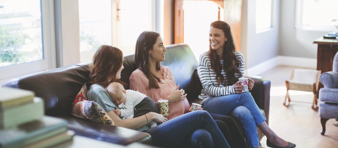 Pregnant woman with friends and baby boy on sofa